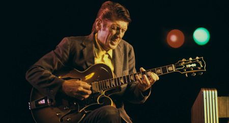 Jazz great Tal Farlow plays his Gibson hollowbody onstage at Newport, wincing as he plays a run.