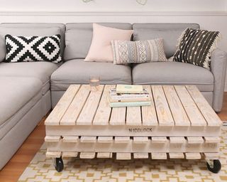 A natural pallet coffee table on caster wheels in living room with grey sofa and pattered cushion decor