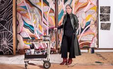 Emma Talbot in front of her artworks, with a trolley of paints