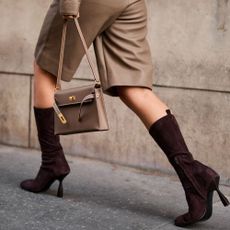 Woman wears trouser shorts and matching beige handbag and calf-hugging boots while walking