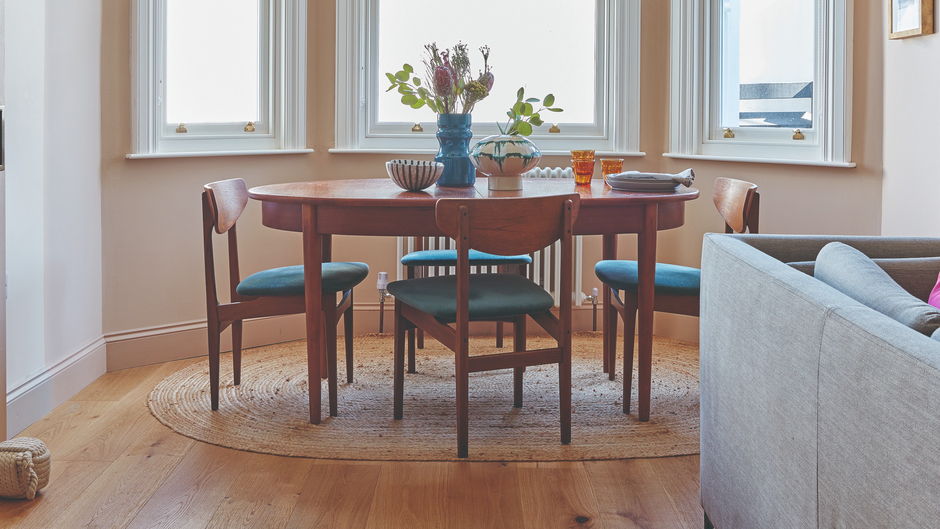 A dining area with an oval midcentury table in dark wood with matching dining chairs and an oval jute rug underneath