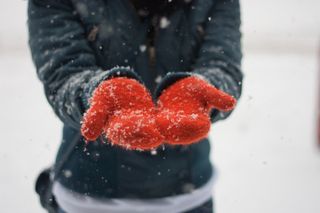 A person wearing a black coat and red fluffy gloves in the snow