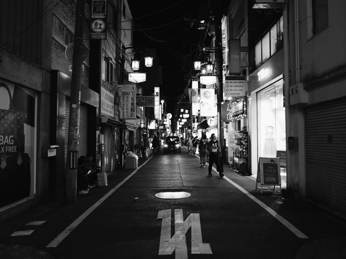 Black-and-white photo of a narrow Osaka street at night.