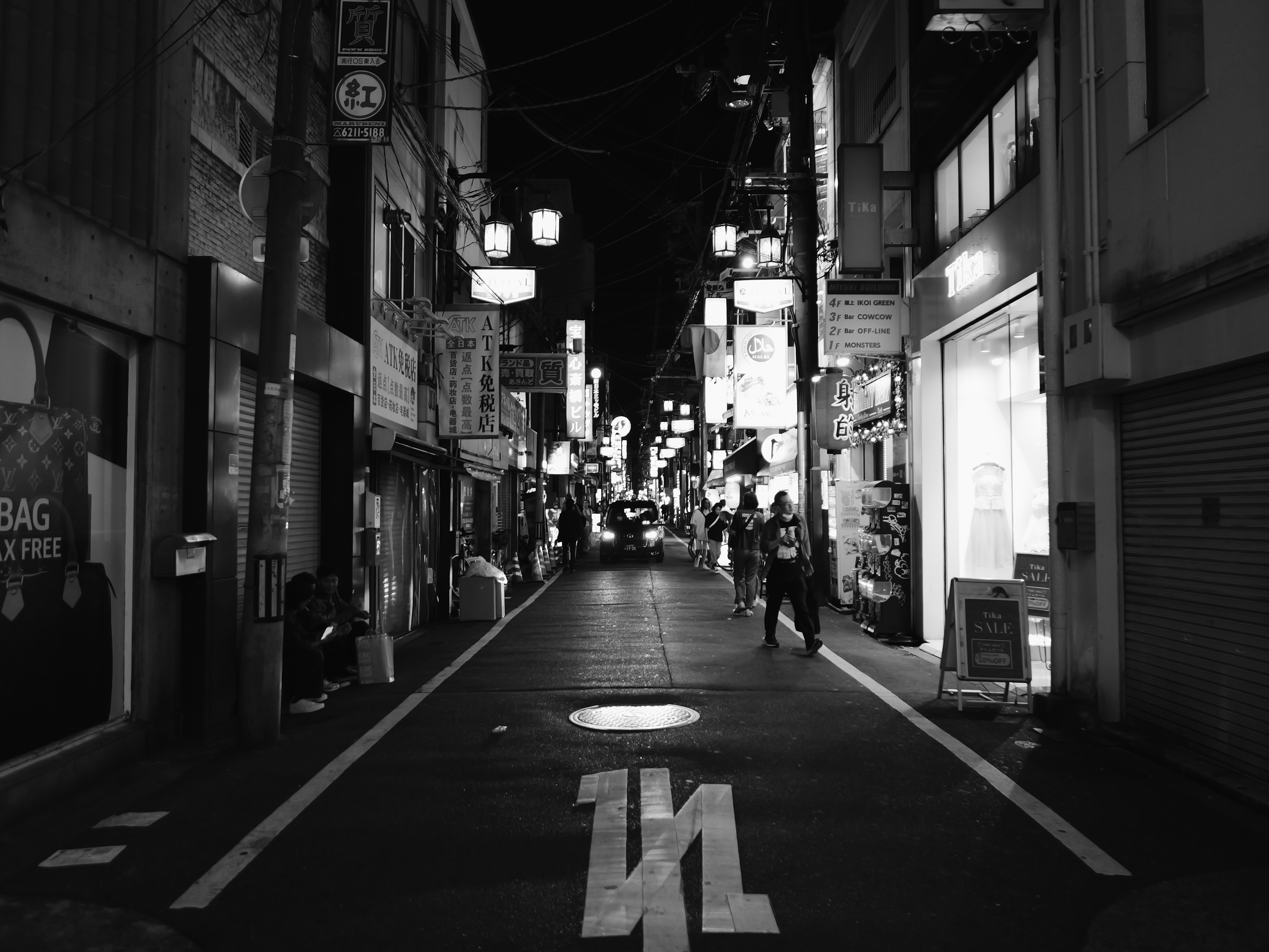 Black-and-white photo of a narrow Osaka street at night.