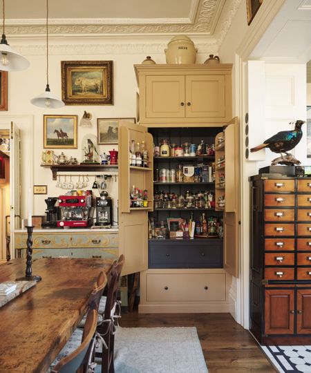 Traditional deVOL kitchen featuring a freestanding pantry cupboard with internal spice racks and drawer storage, set alongside a farmhouse dining table, antique furnishings and decorative wall art.