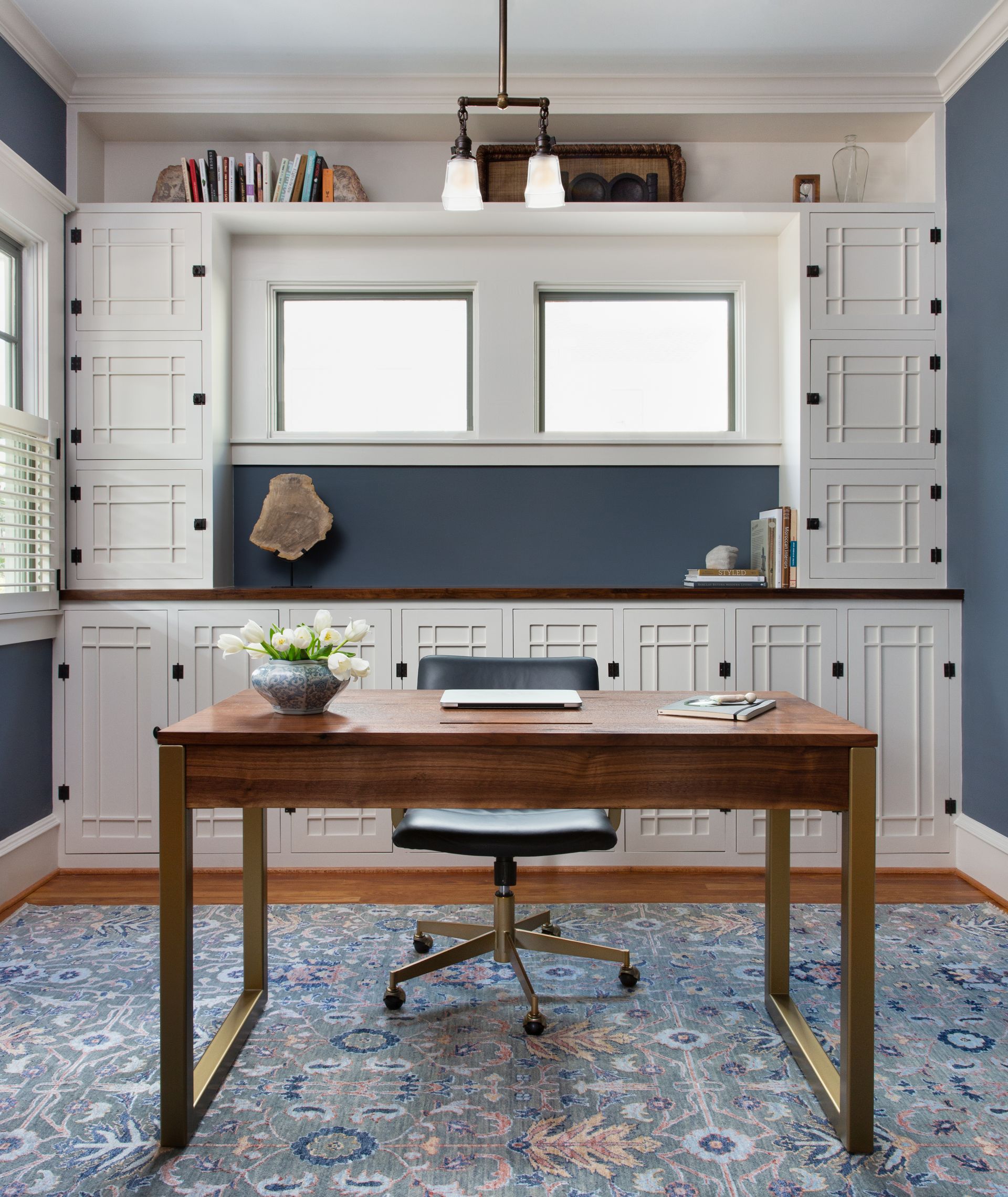 Home office with desk and chair and built in cabinetry behind, blue walls and rug