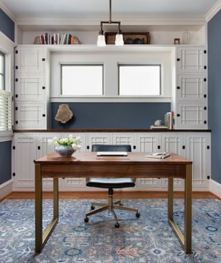 Home office with desk and chair and built in cabinetry behind, blue walls and rug