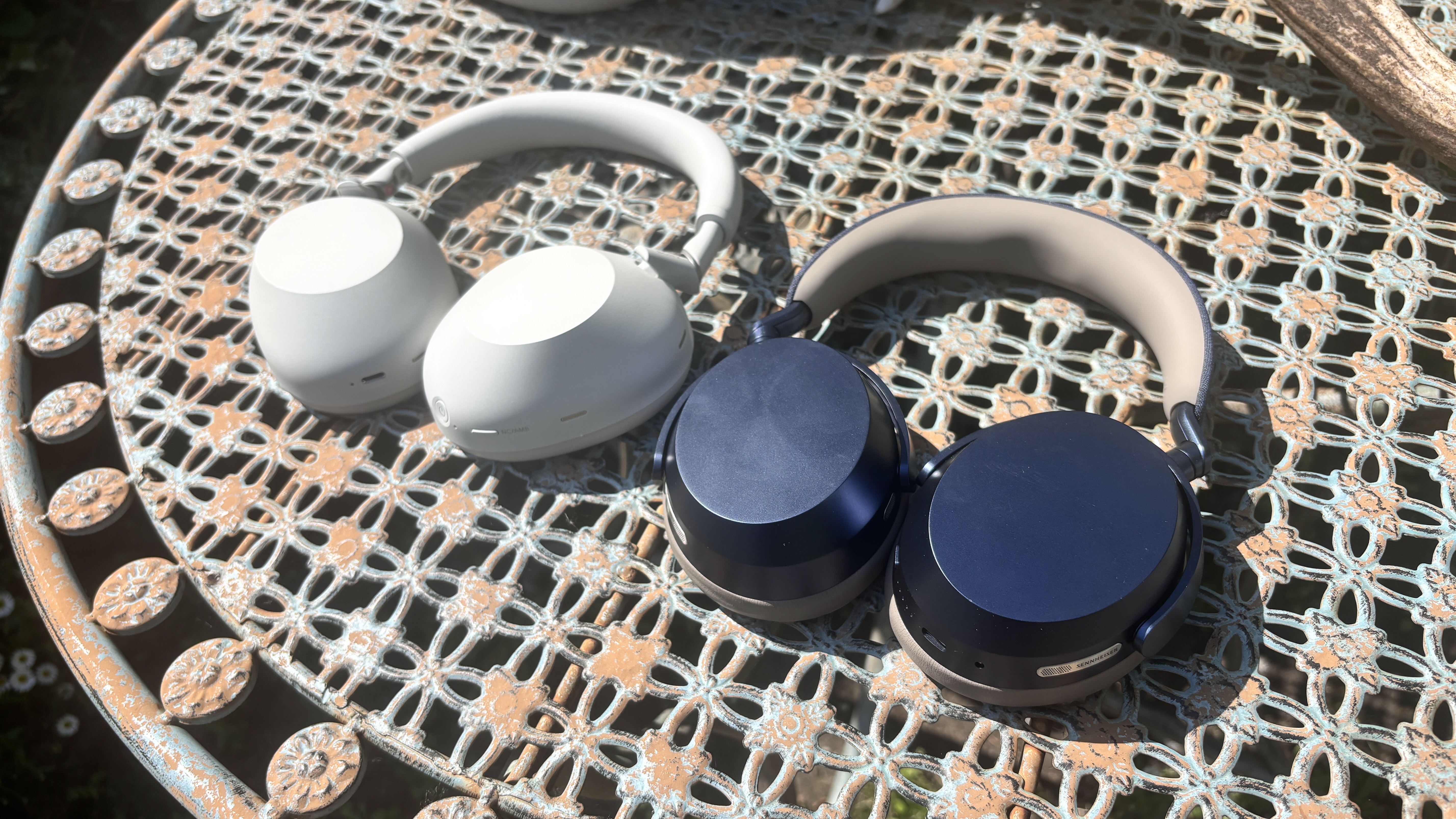 Sony WH-1000XM6 and Sennheiser Momentum 5 Wireless headphones placed side by side on a table outside