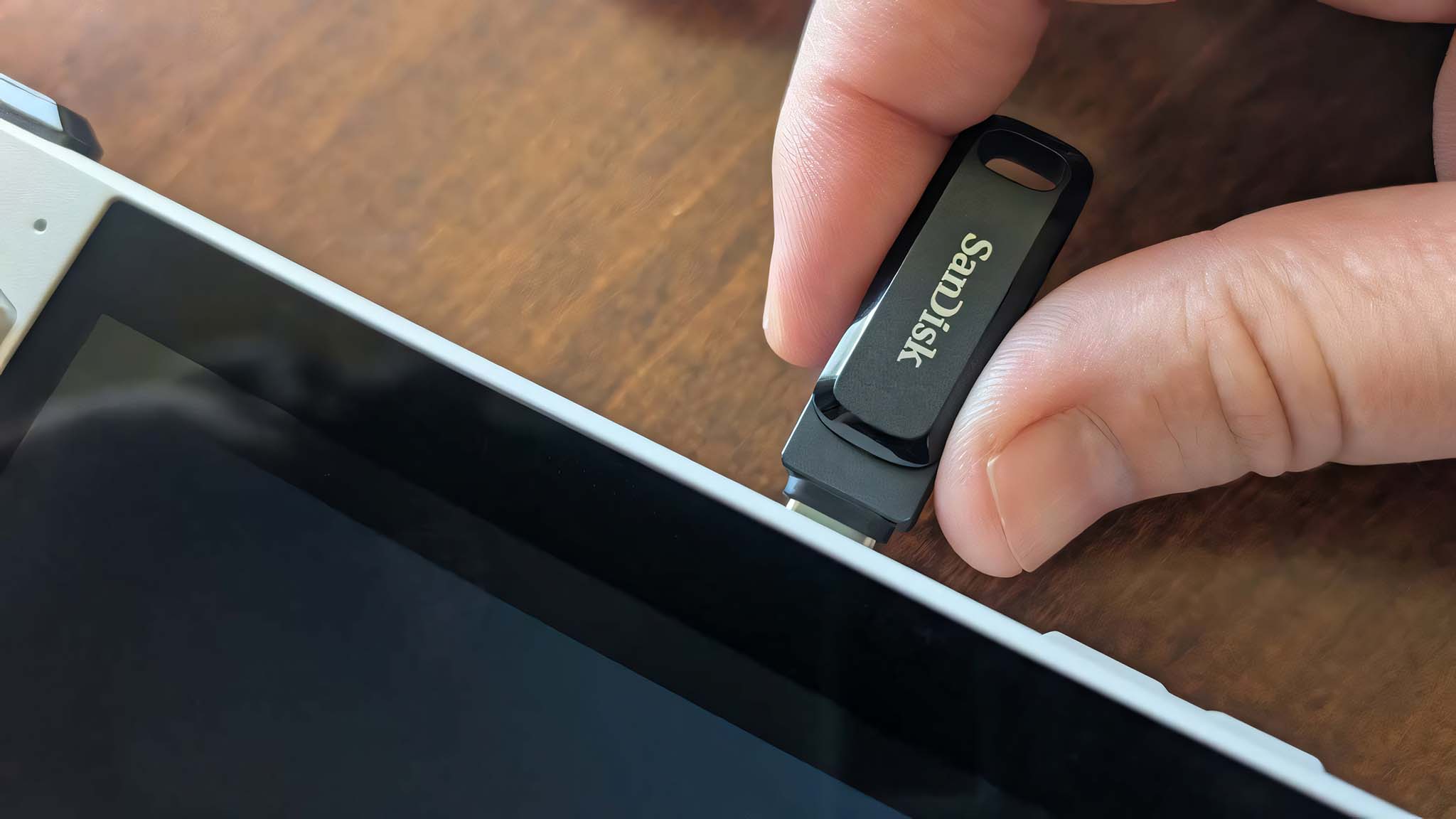 Two fingers pushing a SanDisk flash drive into the top of the ROG Ally.