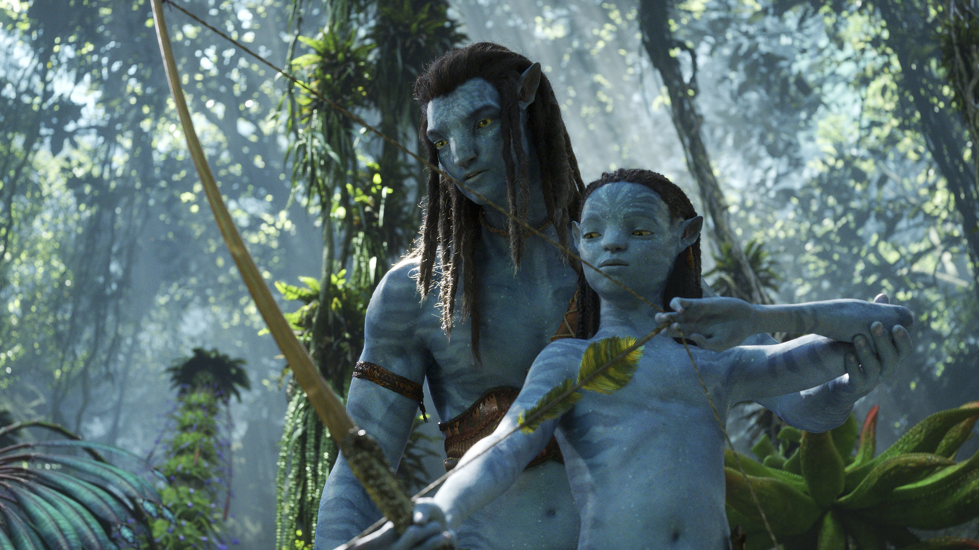 Jake stands over Kiri as she aims an arrow at a fish off-camera in Avatar: The Way of Water