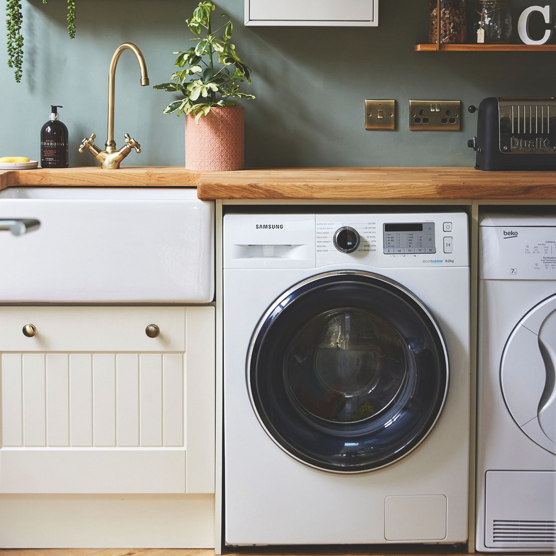 Utility area with wooden worktop, a white ceramic sink and cream cabinets next to a white washing machine