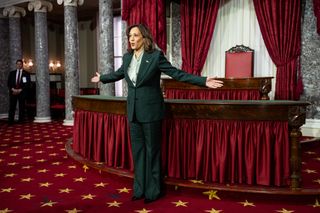 Kamala Harris wearing a green suit with her arms outstretched in front of a red carpeted room