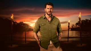 Joel Dommett photographed in front of lit torches on a beach at sundown for Survivor UK 2023