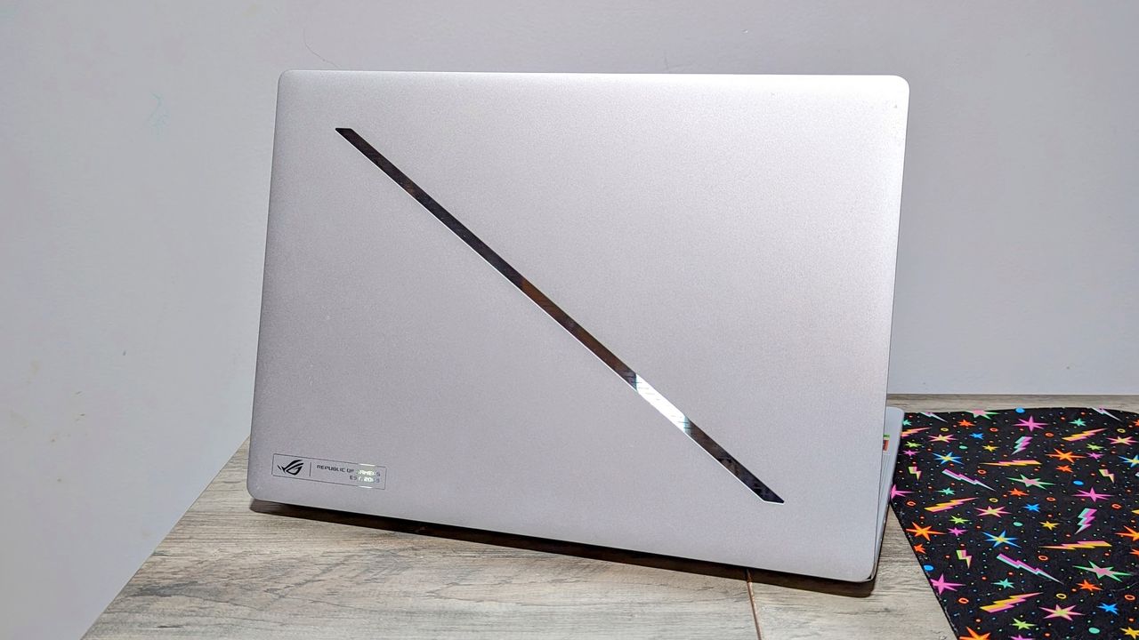 Asus Zephyrus G14 (2024) open on a brown table, highlighting the silver lid and the diagonal LED slash in the center.