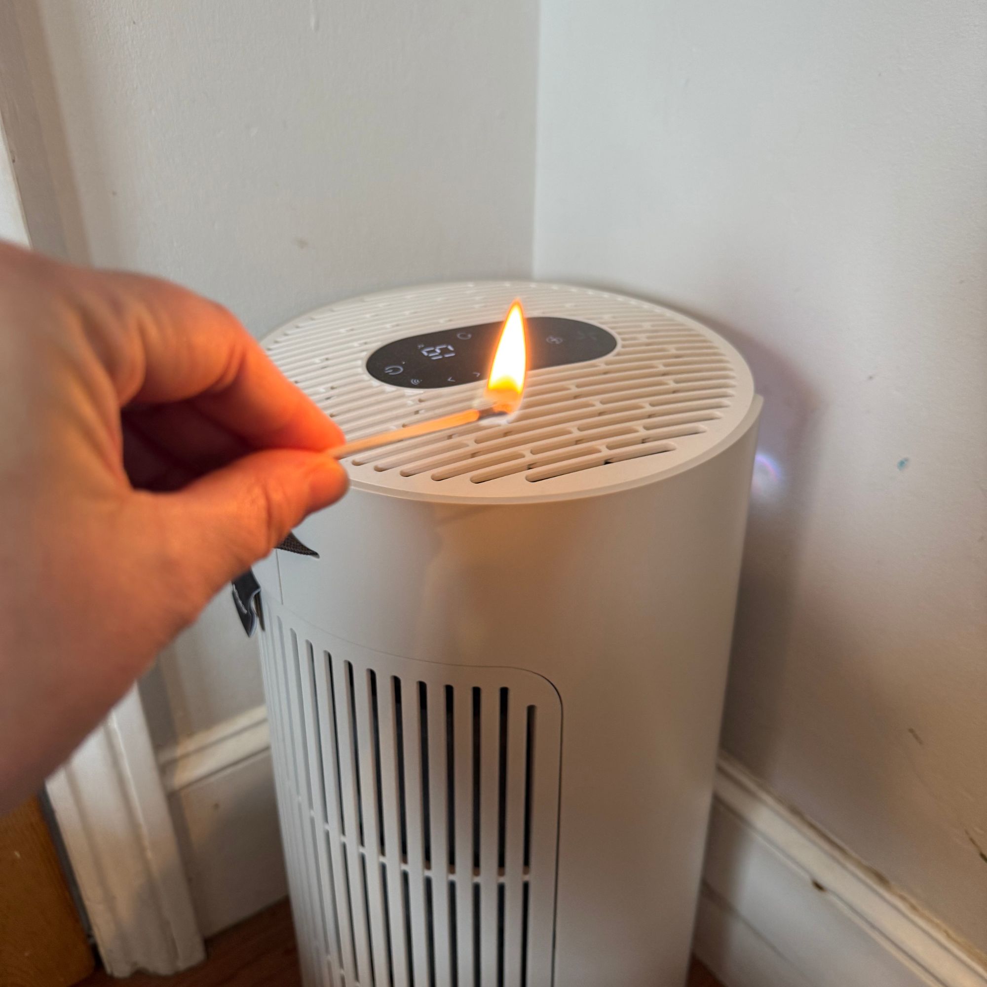 A hand holding a lit match in front of the Blueair ComfortPure 3-in-1 T10i Air Purifier