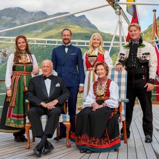 King Harald, Queen Sonja, Crown Prince Haakon, Crown Princess Mette-Marit, Princess Ingrid Alexandra, Prince Sverre Magnus pose for a group photo aboard the kingship Norway with mountains in the background