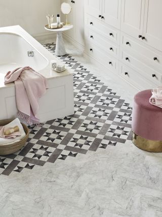 Bathroom with white cabinets, bath, and LVT flooring with geometric pattern around bath and herringbone marble effect beyond