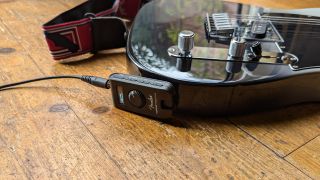 A Fender Mustang Micro Plus plugged into a Telecaster guitar lying on a wooden floor