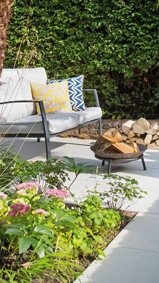 Outdoor sofa with colourful cushions on a stone path with a firepit