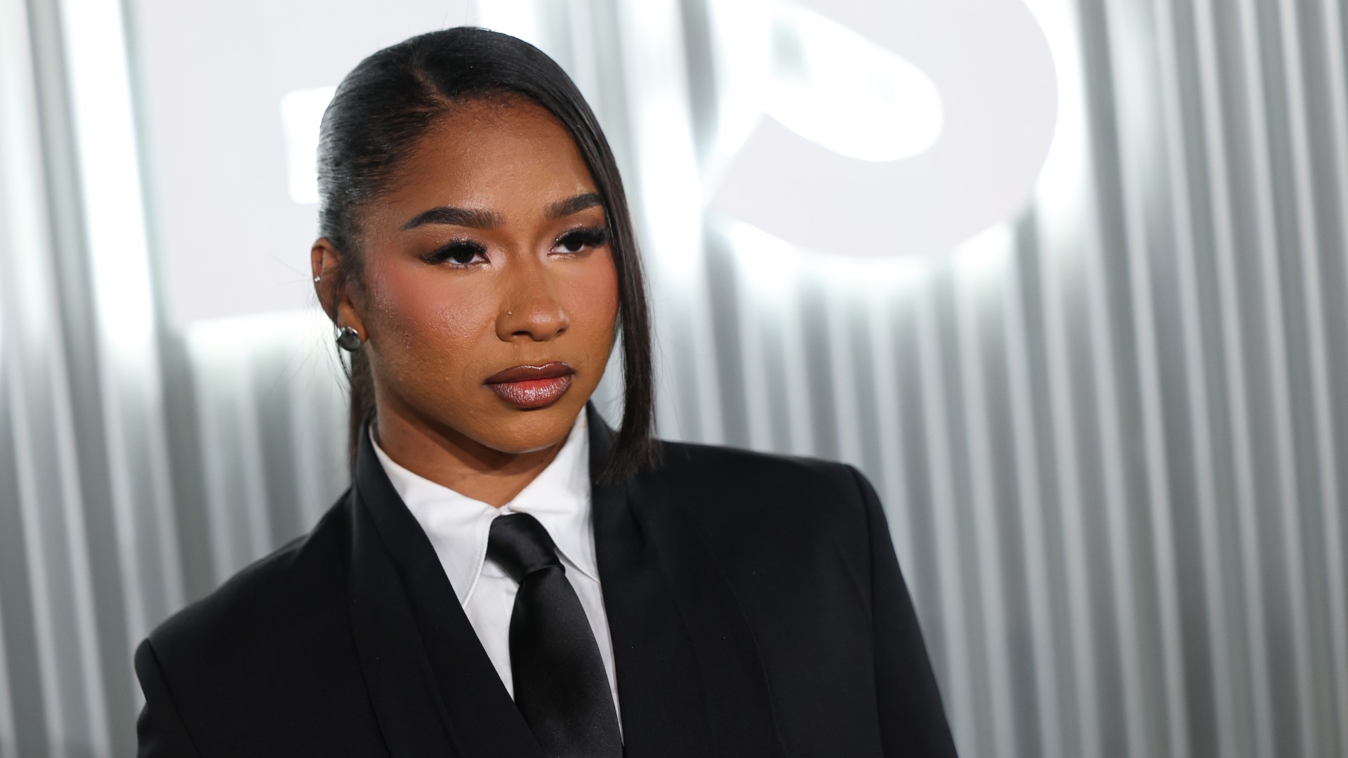 a black woman with dark hair wears a black suit in front of a white background