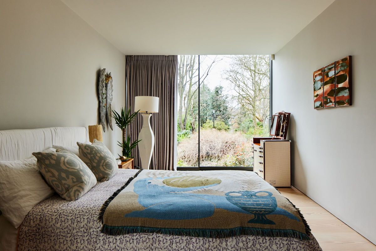 A bedroom on the second floor has a large glass wall looking out onto the surrounding park