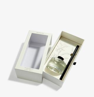 A reed diffuser in a cream box against a white background.