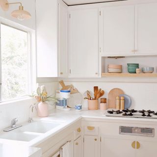 Airy, bright kitchen with white cabinets, brass hardware, and coral and blush kitchen accessories on counters.