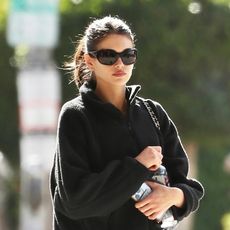 Kaia Gerber wearing a black fleece pullover with black leggings and black sneakers