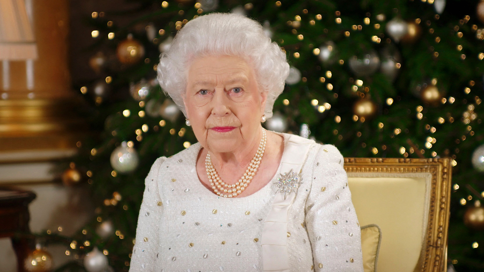 Queen Elizabeth wearing a white dress sitting in front of a Christmas tree