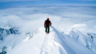 Climber on steep, exposed snowy summit of Europe's tallest peak, Mt Blanc