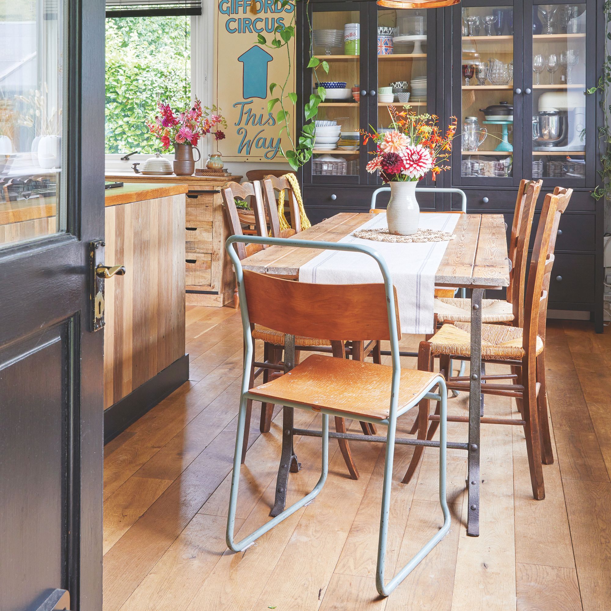 A dining area with mixed and matched chairs and a black display cabinet connected to the kitchen