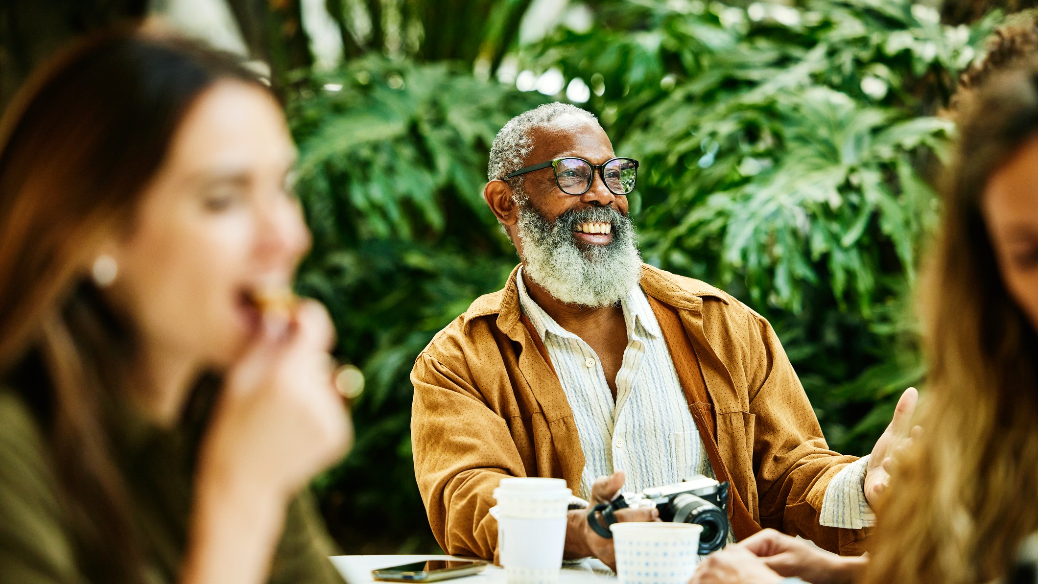 Medium shot of smiling senior man relaxing at outdoor caf&eacute; during vacation in city.