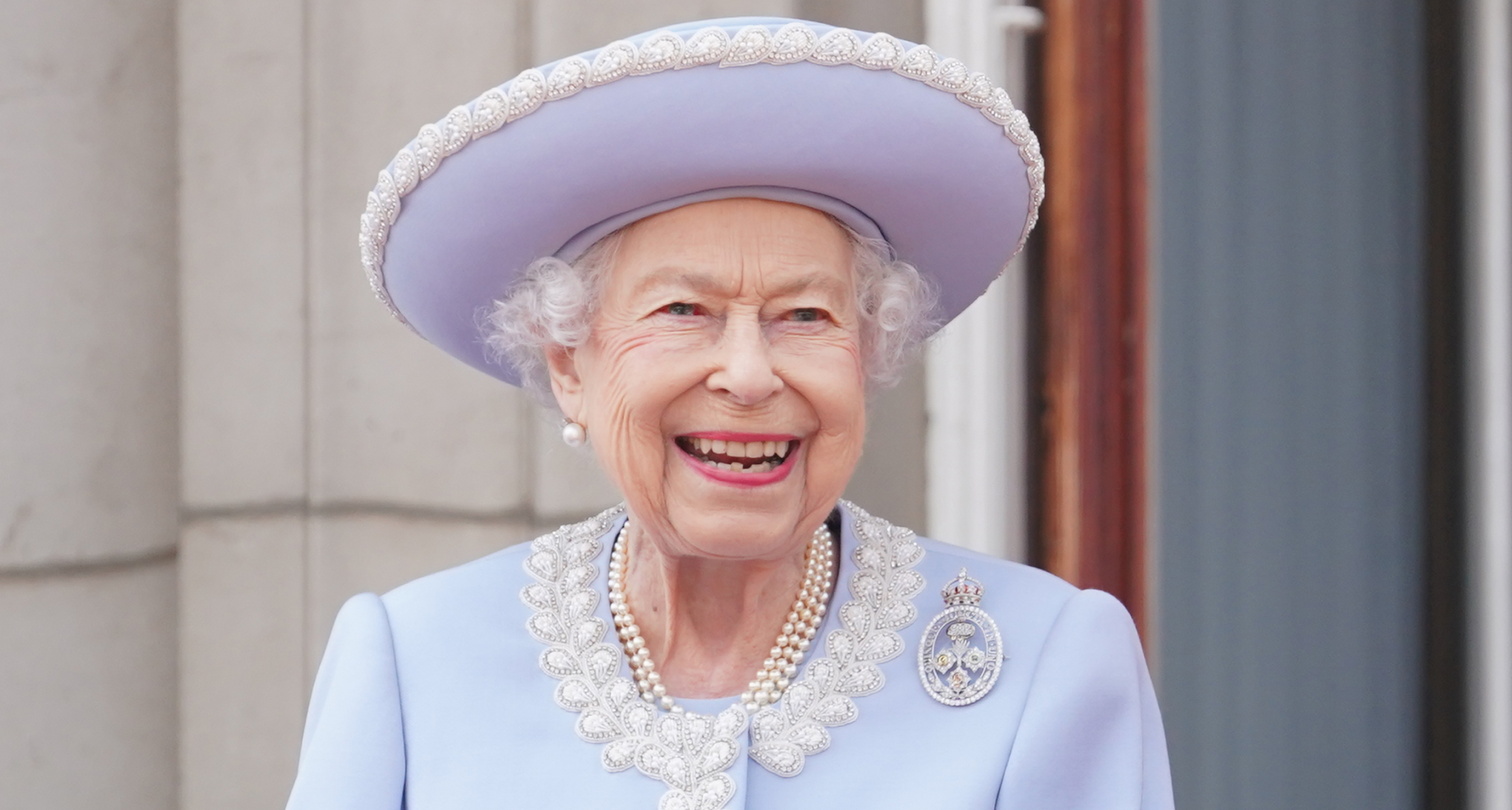 Queen Elizabeth wearing a blue coat and hat smiling