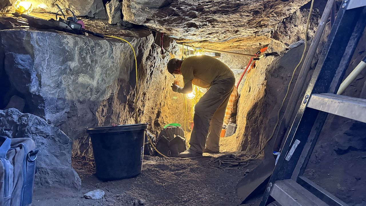a man works by flashlight at an excavation site in a cave