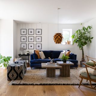 White living room with a blue sofa, gallery wall art, money tree in pot, ikat pouffes and wood coffee tables