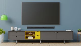 The Groov-e soundbar 160 pictured affixed to a wall underneath a large TV in a tastefully decorated living room with blue walls