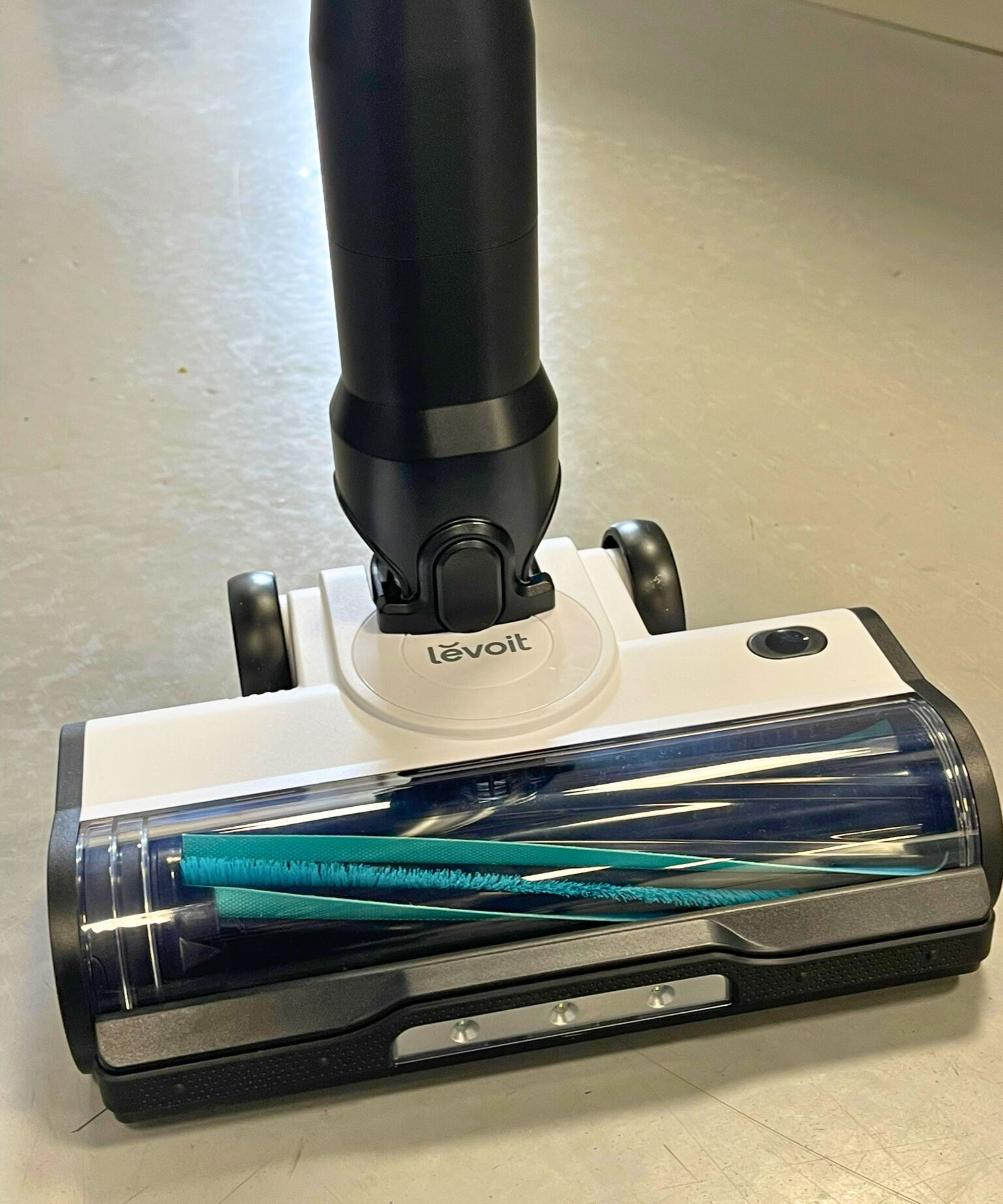 Closeup of the Levoit AERO cordless vacuum's floorhead on gray floor. The floorhead has blue fins and bristles at a diagonal angle.