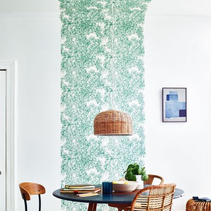 White dining room with strip of green patterned wallpaper leading up and onto ceiling 