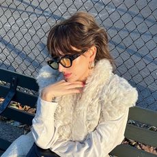 a woman wearing a white fur jacket, black framed glasses and wedge sneakers