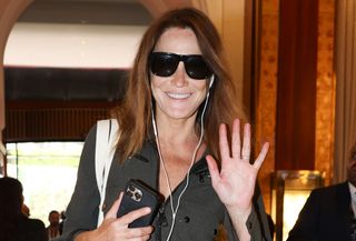 Carla Bruni is seen at Le Majestic Hotel during the 77th Cannes Film Festival wearing a utility jumpsuit, a YSL quilted-leather tote bag, oversize sunglasses, and flat thong sandals.