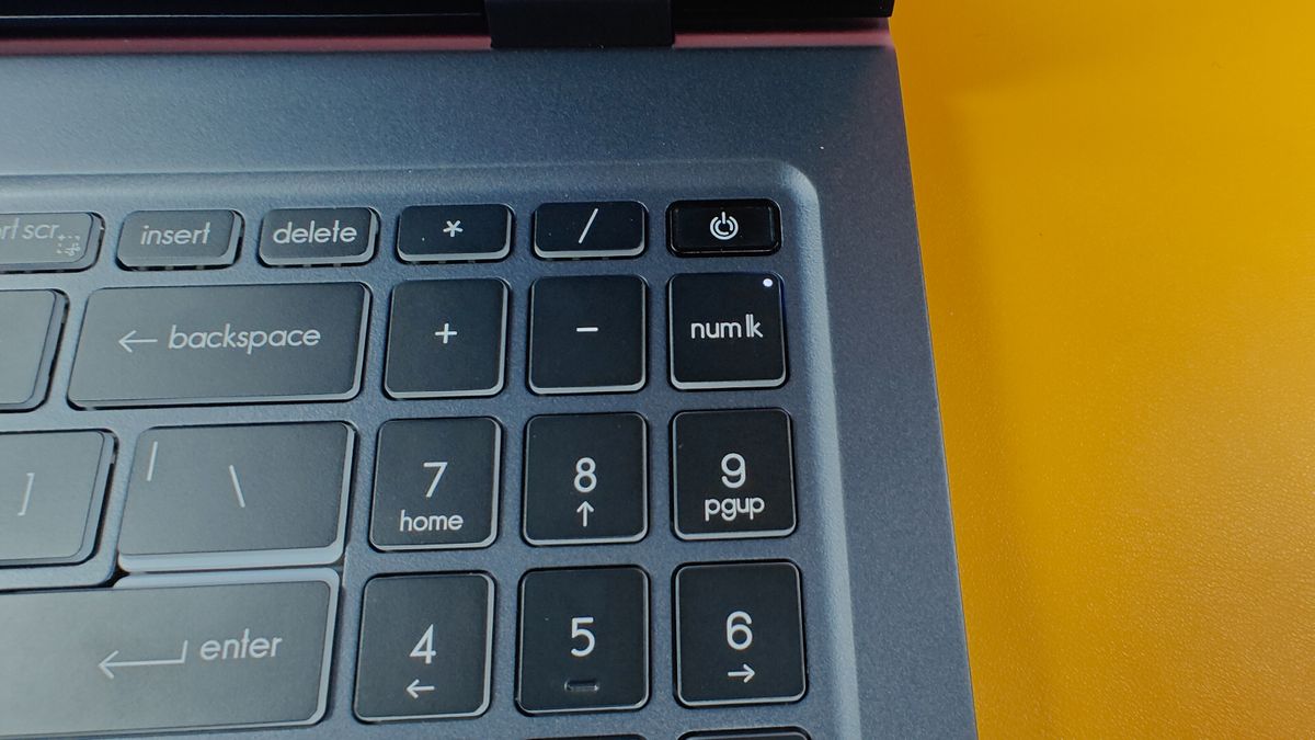 A close up of the number keys and power button on a laptop against a mustard-yellow background.