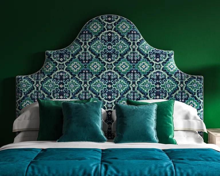 A dark green bedroom with a large upholstered headboard in a blue, white and green patterned velvet