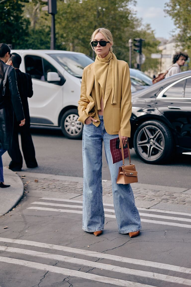 a woman at fashion week wearing blue jeans and a yellow jacket and scarf