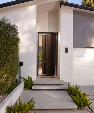 A modern, white home with sleek steps leading to an open, black front door