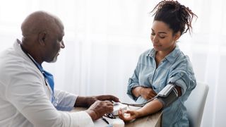 Young pregnant black woman sits across from a doctor as he takes her blood pressure with a blood pressure cuff