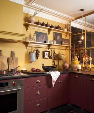 an English shaker kitchen with burgundy red cabinets and warm yellow walls with open shelves and many styling objects