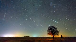 the next meteor shower could produce a dazzling display like the one in this photo of the Geminids. The image shows a sky full of shooting stars above a tree and a lone person.