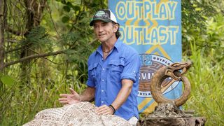 Jeff Probst standing over a cloth covered table on Survivor