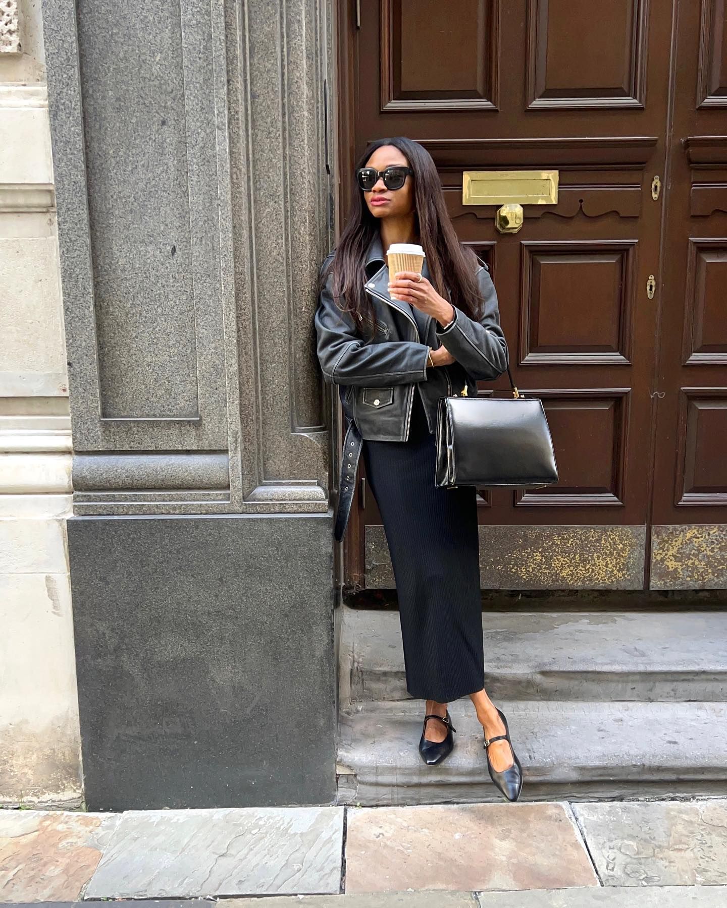 @symphonyofsilk wears a black leather jacket, black midi dress and mary jane flat shoes