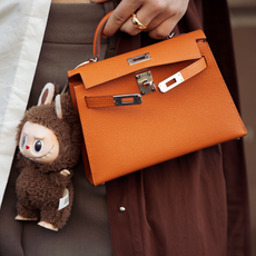 Woman wearing luxury handbag with Labubu bag charm.